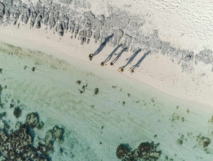 vue 90° d'une famille se baladant sur la plage de Tetiaroa, ombres projetées par le soleil sur le sable - Voyage en Famille en Polynésie