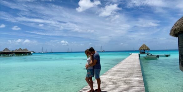 couple s'enlaçant sur un ponton à Rangiroa. Lagon turquoise et pilotis en arrière fond - voyage de noces polynésie