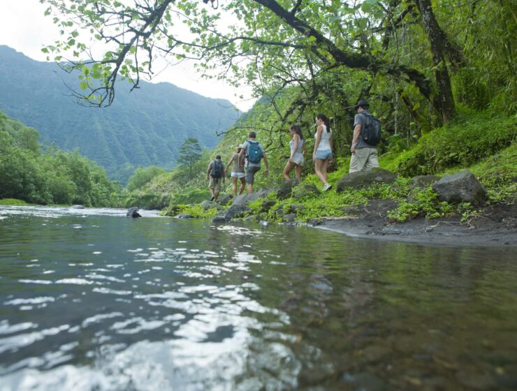 groupe de six randonneurs marchant le long d'une rivière dans la vallée de la papenoo à Tahiti. Montagne verte en arrière plan. Randonnée et Aventure en Polynésie : Les Meilleurs Sentiers et Conseils de Sécurité