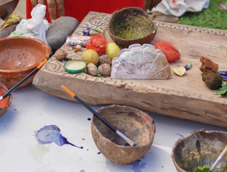 Atelier de fabrication de peintures naturelles à Tahiti. 4 noix de coco avec peintures naturelles et pinceaux posés sur une table. Immersion dans l'Art Polynésien : Tatouages, Sculptures, et Peintures.