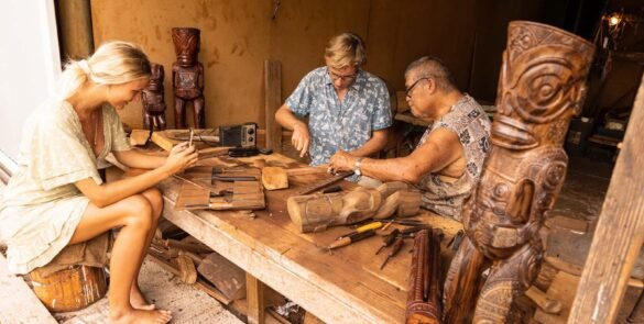 couple apprenant à sculpter avec un marquisien à Nuku Hiva. Tiki en bois au premier plan.