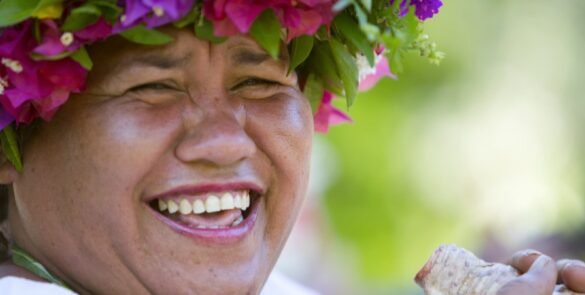portrait d'une femme polynésienne riant avec une couronnes de fleurs sur la tête.