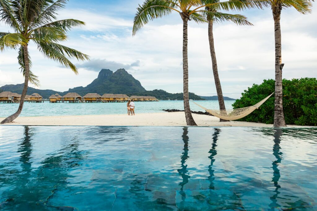 piscine à débordement au premier plan avec un couple sur la plage se prélassant et regardant le Mont Otemanu situé en arrière plan