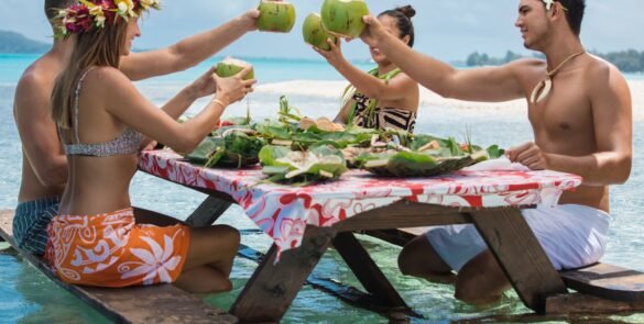 Locaux et touristes trinquant avec une noix de coco "Manuia" attablé dans un lagon en Polynésie