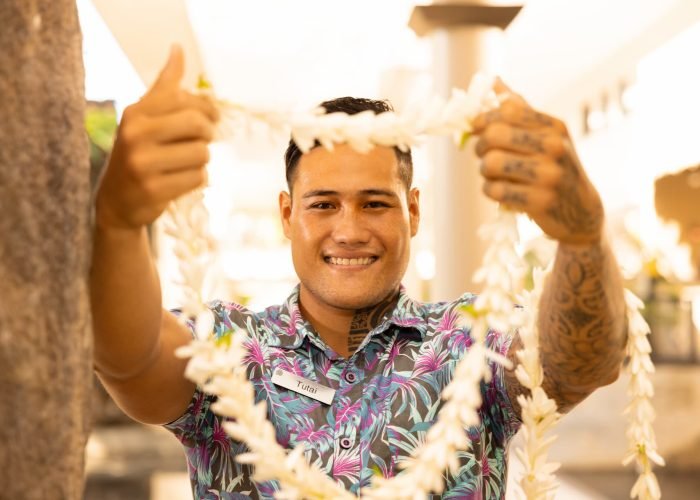 homme polynésien qui tend un collier de fleurs de tiare.