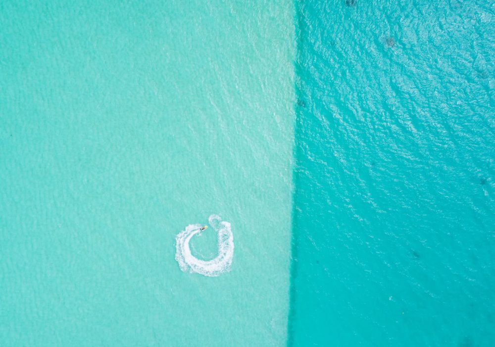 Vue aérienne 90° du lagon de Bora Bora, deux couleurs d'eau turquoise différentes, un jet ski faisant une boucle