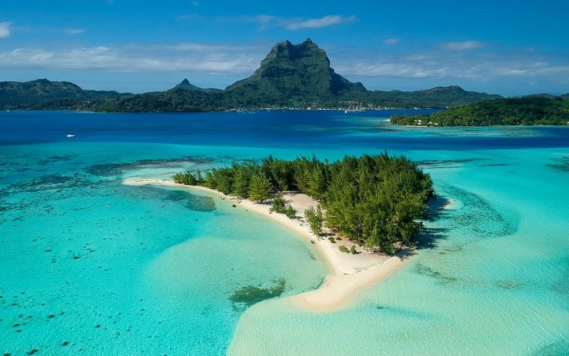 vue aérienne du lagon de Bora Bora avec un motu en premier plan et le mont Otemanu en arrière plan