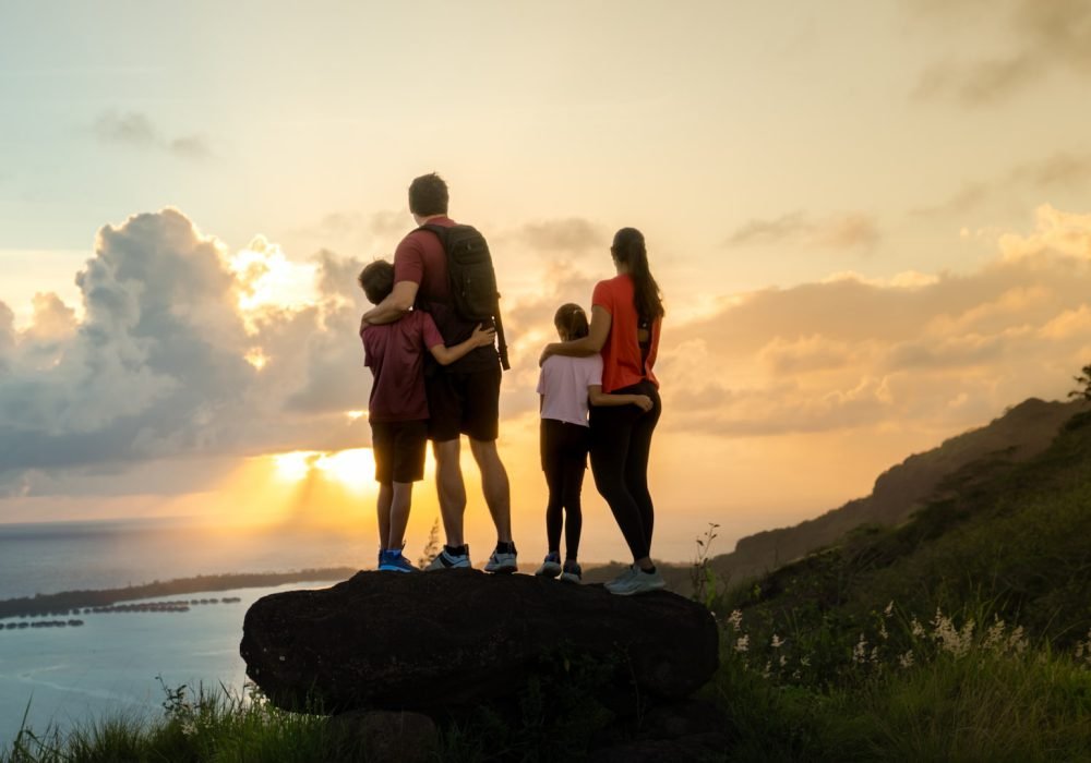 Famille de 2 adultes et 2 enfants de dos, en haut d'une montagne à Bora bora au coucher du soleil