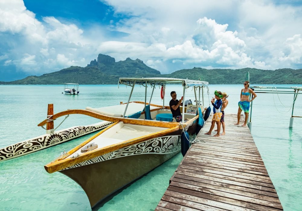 pirogue polynésienne accostée sur un ponton à Bora Bora, famille avec deux enfants en maillot de bain sur le ponton, Mont Otemanu en arrière-plan