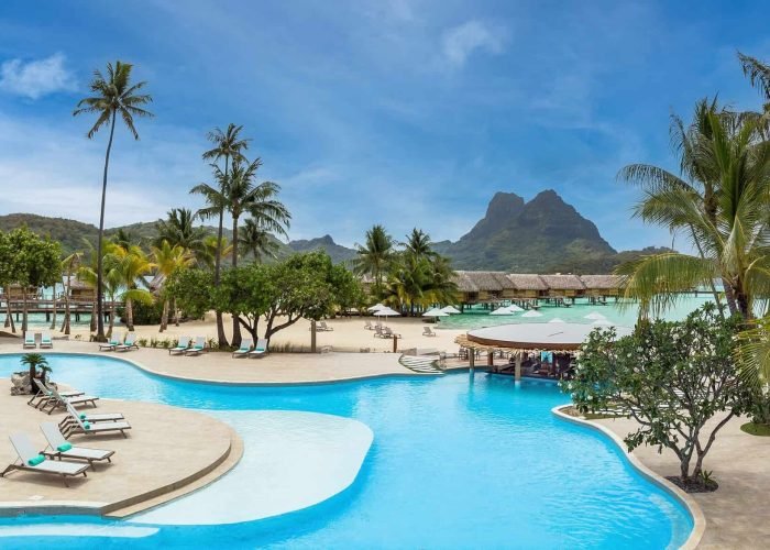 Hôtel Le Hôtel Le Bora Bora by Pearl Resorts 5*. Vue sur la piscine, la plage, les bungalows sur pilotis. Montagne en arrière plan.