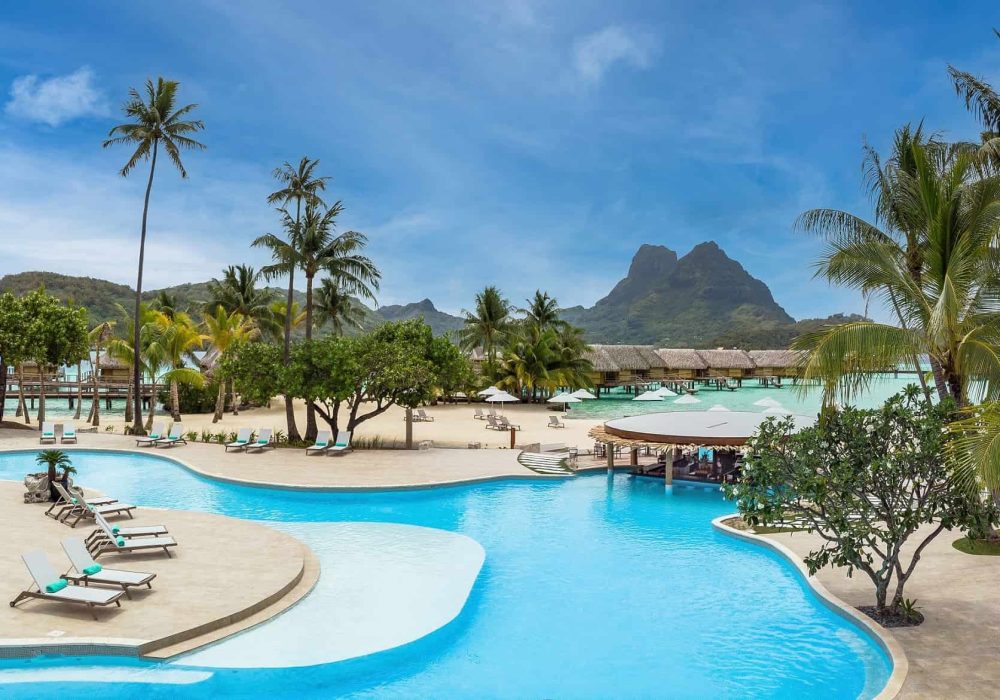 Hôtel Le Hôtel Le Bora Bora by Pearl Resorts 5*. Vue sur la piscine, la plage, les bungalows sur pilotis. Montagne en arrière plan.