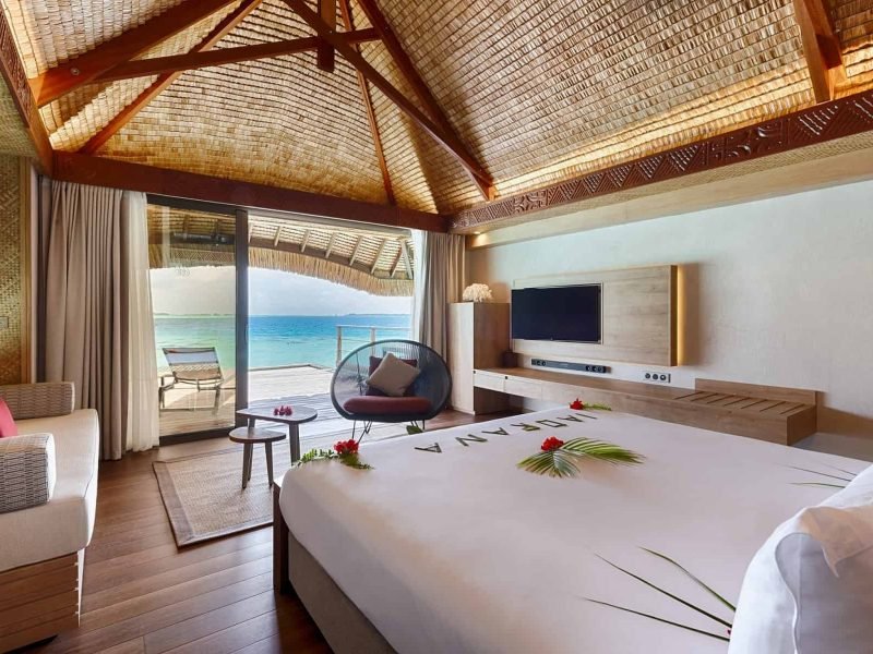 Hôtel Le Bora Bora by Pearl Resorts n4*. Vue de l'intérieur d'un bungalow sur pilotis, avec lit face au lagon.