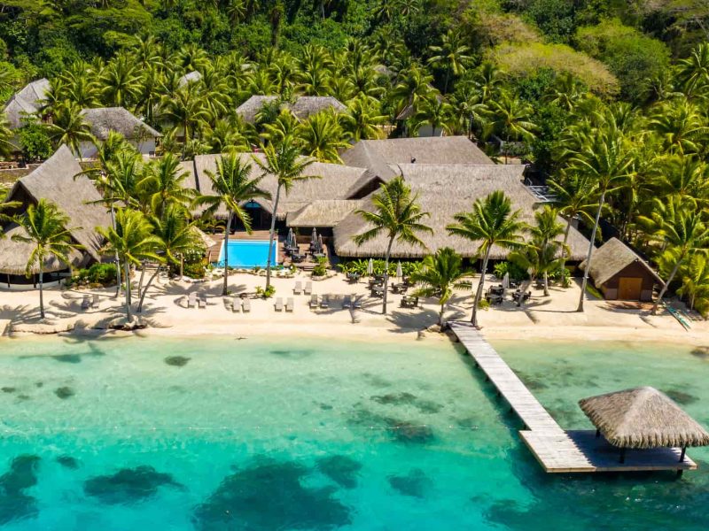 Hôtel Royal Bora Bora 3*. Vue aérienne sur le lagon, le ponton et les installations de l'hôtel avec la piscine. Montagne et cocotiers en arrière plan.