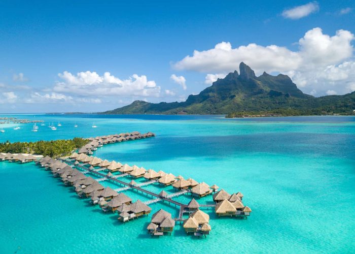 Hôtel St Regis 5* à Bora Bora - Vue aérienne des villas sur pilotis, lagon turquoise, et Mont Otemanu.