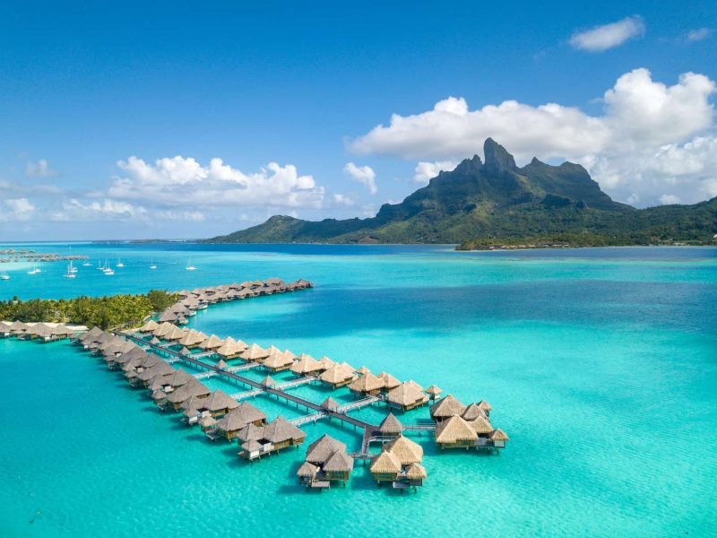 Hôtel St Regis 5* à Bora Bora - Vue aérienne des villas sur pilotis, lagon turquoise, et Mont Otemanu.