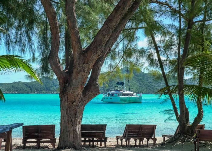 subtiles-tahiti-croisiere-catamaran-dream-yacht-charter-14©dream-yacht-charter Croisière Dream Yacht Chater - Vue depuis la plage d'un catamaran Lagoon 620 sur un lagon turquoise en Polynésie française.