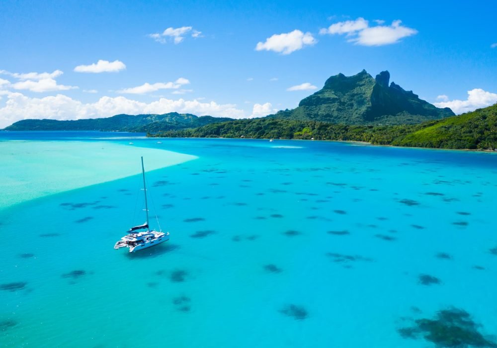 vue aérienne d'un catamaran Lagoon 620 de Dream Yacht Charter, lagon turquoise et montagne