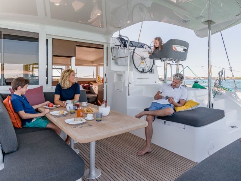 Croisière privative avec Tahiti Yacht Charter. vue de l'arrière d'un catamaran Lagoon 40, avec une famille prenant un petit-déjeuner sur le deck extérieur.