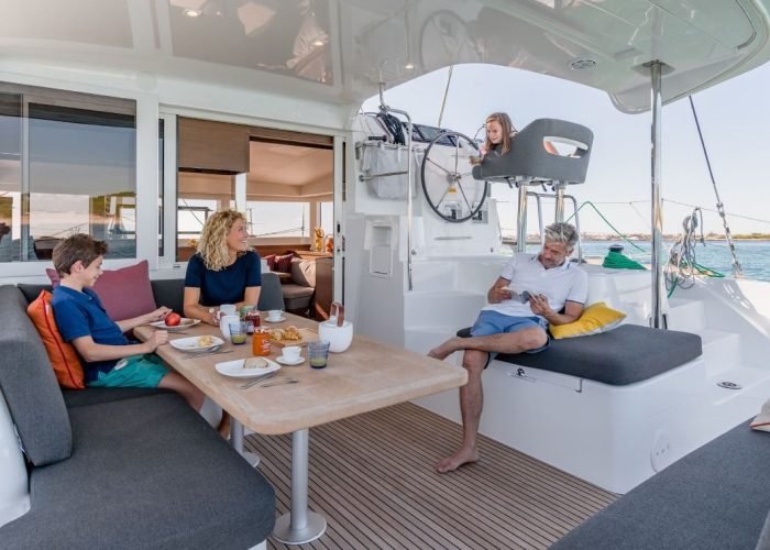 subtiles-tahiti-croisiere-catamaran-tahiti-yacht-charter-3©nicolas-claris Croisière privative avec Tahiti Yacht Charter. vue de l'arrière d'un catamaran Lagoon 40, avec une famille prenant un petit-déjeuner sur le deck extérieur.