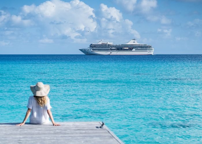 Croisière Paul Gauguin – Ponant - femme assis sur un ponton à Rangiroa face au lagon, avec le Paul Gauguin en arrière plan