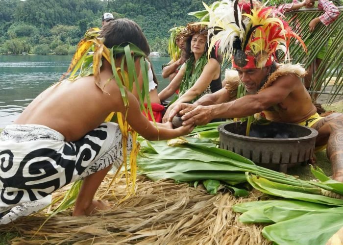 couple avec un enfant assis sur la plage, en costume traditionnel polynésien - Écotourisme en Polynésie : à la découverte de la nature préservée.
