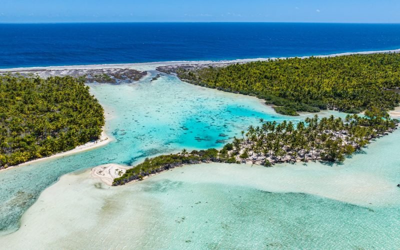 vue aérienne de motus parsemés de cocotiers à Fakarava, avec la barrière de corail faisant frontière entre l'océan et le lagon turquoise