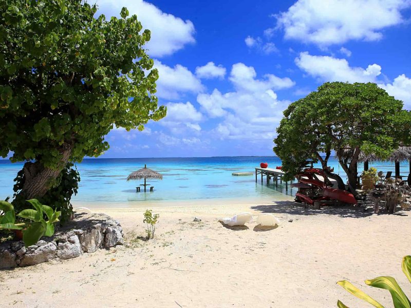 Pension Havaiki Lodge à Fakakara. Vue sur la plage et le lagon. Ponton et table et parasol dans l'eau.