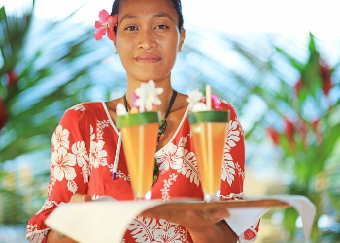 Hôtel Hanakee Lodge 3* à Hiva Oa – Femme polynésienne tenant un plateau avec 2 cocktails de bienvenue.