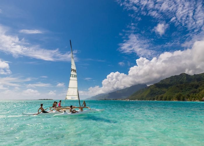 6 personnes naviguant sur une pirogue à voile et à balancier, sur le lagon turquoise de Moorea.