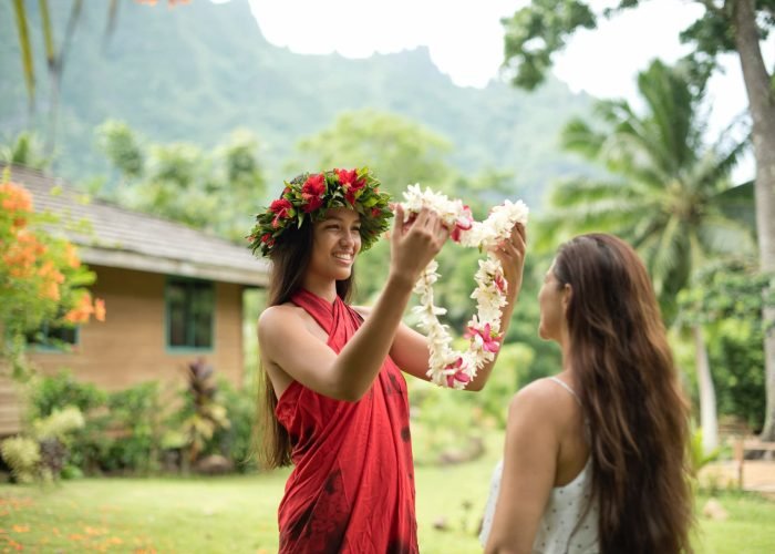 jeune femme polynésienne avec une couronne de fleurs mettant un collier de fleurs de bienvenue à une touriste