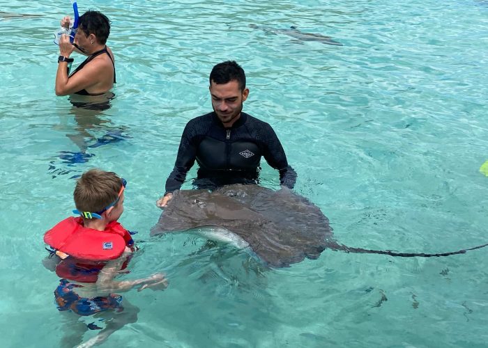 Enfant s'approchant d'une raie pastenague dans le lagon de Moorea.