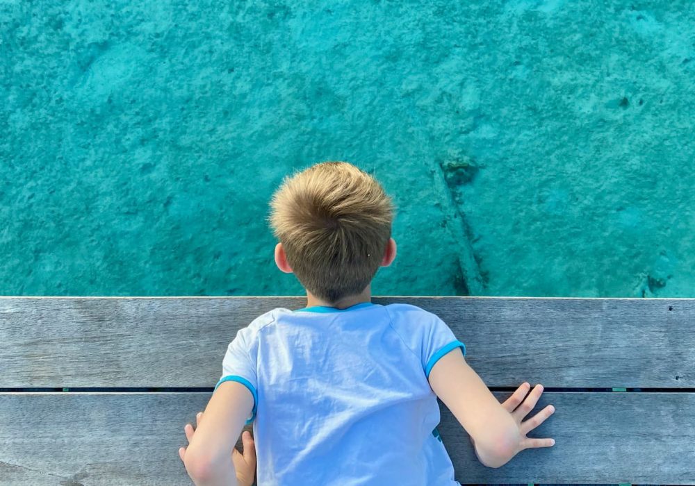 enfant allongé sur le ventre sur un ponton regardant les poissons dans le lagon turquoise de Moorea