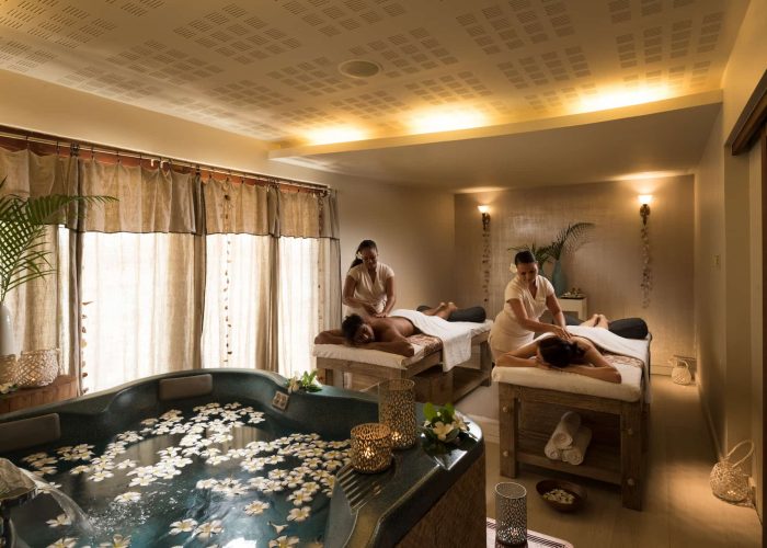 Hôtel Hilton Lagoon Resort & Spa 5* à Moorea. Couple se faisant masser par deux femmes tahitienne au Spa de l'hôtel. Jacuzzi avec fleurs de tipaniers au premier plan.