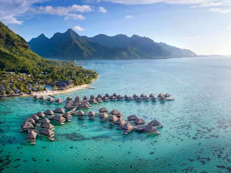 Hôtel Hilton Lagoon Resort & Spa 5* à Moorea. Vue aérienne générale sur l'hôtel, le lagon, et les bungalows sur pilotis. Montagnes de Moorea en arrière plan.