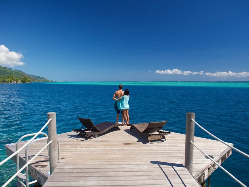 Couple de dos entrelacés sur le bout du ponton à l'hôtel Manava Beach Resort & Spa 4* à Moorea. Lagon et montagne et arrière-plan.