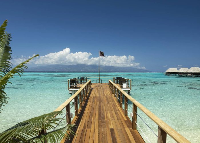 Hôtel Sofitel Kia Ora Beach Resort 4*. Vue sur le ponton du restaurant Pure. Lagon et île de Tahiti en arrière plan. Bungalows sur pilotis horizon sur la droite.