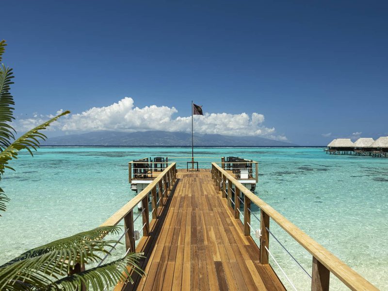 Hôtel Sofitel Kia Ora Beach Resort 4*. Vue sur le ponton du restaurant Pure. Lagon et île de Tahiti en arrière plan. Bungalows sur pilotis horizon sur la droite.