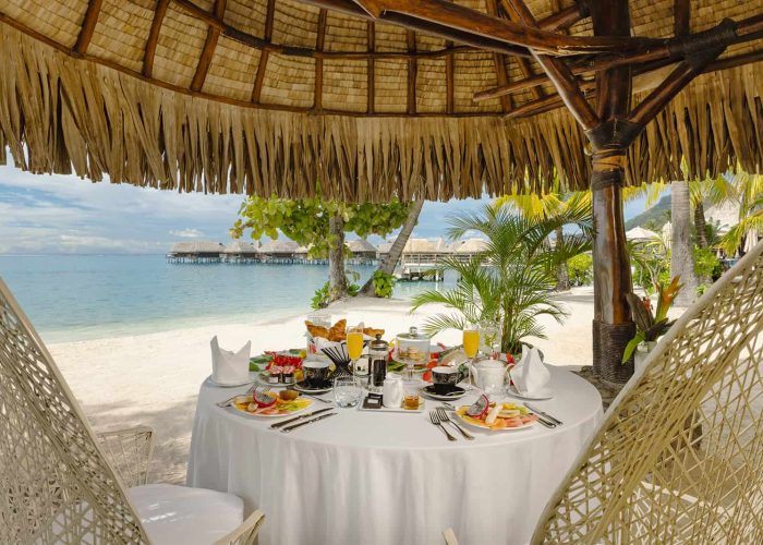 Hôtel Sofitel Kia Ora Beach Resort 5* à Moorea. Petit-déjeuner privé sur la plage avec lagon et Bungalows sur pilotis en arrière plan.