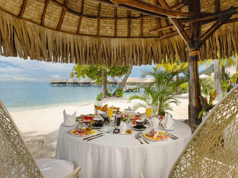 Hôtel Sofitel Kia Ora Beach Resort 5* à Moorea. Petit-déjeuner privé sur la plage avec lagon et Bungalows sur pilotis en arrière plan.