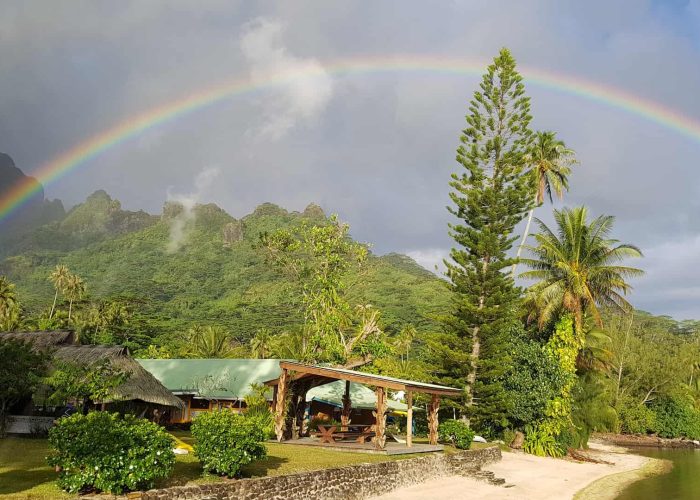 Pension Linareva à Moorea. Vue sur la place et le fare pote de la pension. Montagne et arc en ciel en arrière plan.