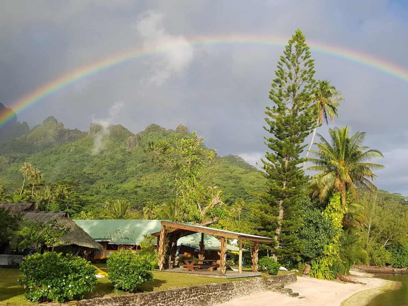 Pension Linareva à Moorea. Vue sur la place et le fare pote de la pension. Montagne et arc en ciel en arrière plan.