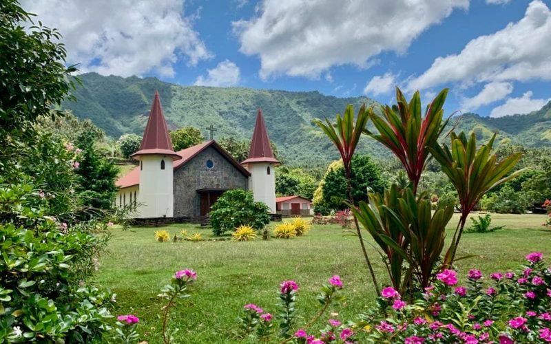Eglise de Hatiheu à Nuku Hiva, avec au premier plan des arbustes fleuris et la montagne en arrière plan