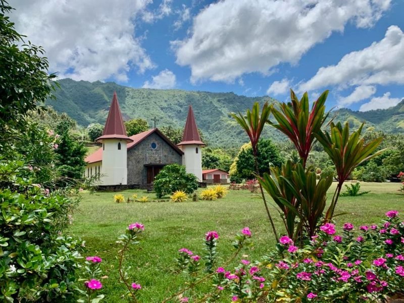Eglise de Hatiheu à Nuku Hiva, avec au premier plan des arbustes fleuris et la montagne en arrière plan