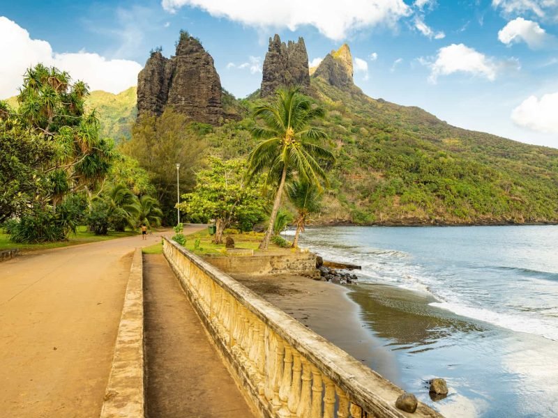 vue sur la plage de Nuku Hiva avec montagne en arrière plan. Un enfant marquisien marche torse nu sur la route.
