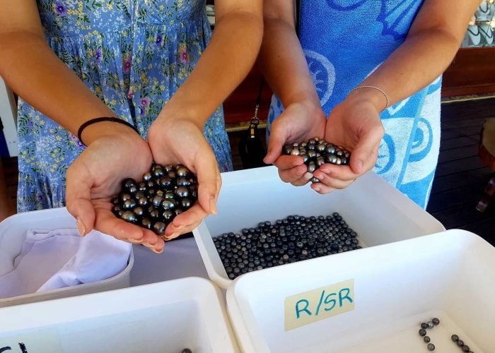 deux femmes polynésiennes tenant aux creux de leurs mains de multiples perles de culture