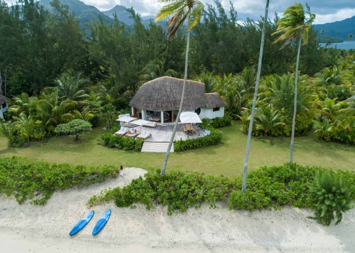 Motu Nao Nao, île privée à Raiatea. Vue aérienne sur une villa dans le jardin du motu. Deux paddles sur la plage de sable blanc.