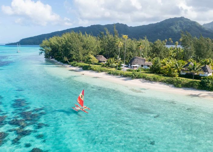 Motu Nao Nao, île privée à Raiatea. Vue aérienne sur le lagon et le motu, avec une pirogue à balanciers au premier plan. Montagnes de Raiatea en arrière plan.