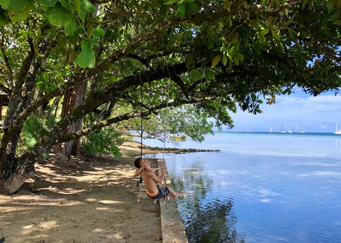 Pension Sunset Beach Motel à Raiatea - bord de lagon avec enfant faisant de la balançoire accrochée à un arbre.