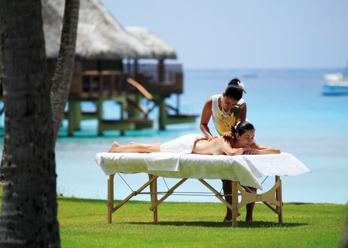 Hôtel Kia Ora Resort & Spa 4* à Rangiroa – Femme Polynésienne massant une cliente dans le jardin de l'hôtel, face au lagon.