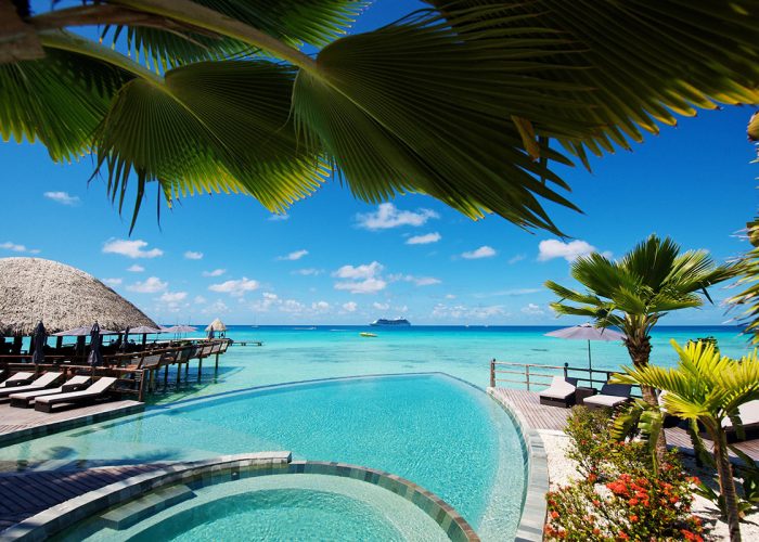 Hôtel Kia Ora 4* à Rangiroa - vue sur la piscine à débordement sur le lagon avec un paquebot en arrière plan. Bar Miki Miki sur pilotis à gauche